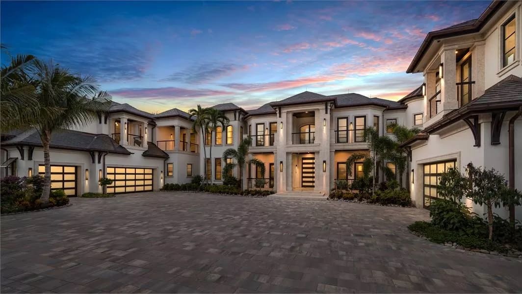 Front view with multiple balconies, a covered entry, and courtyard garages on either side of the house.