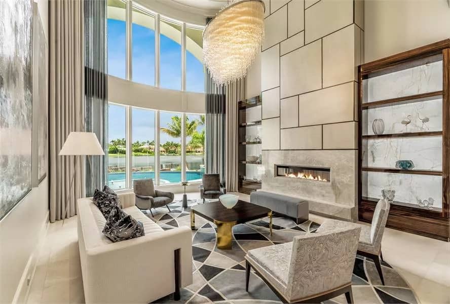 Living room with modern seats, a linear fireplace, and a wall of windows overlooking the swimming pool.