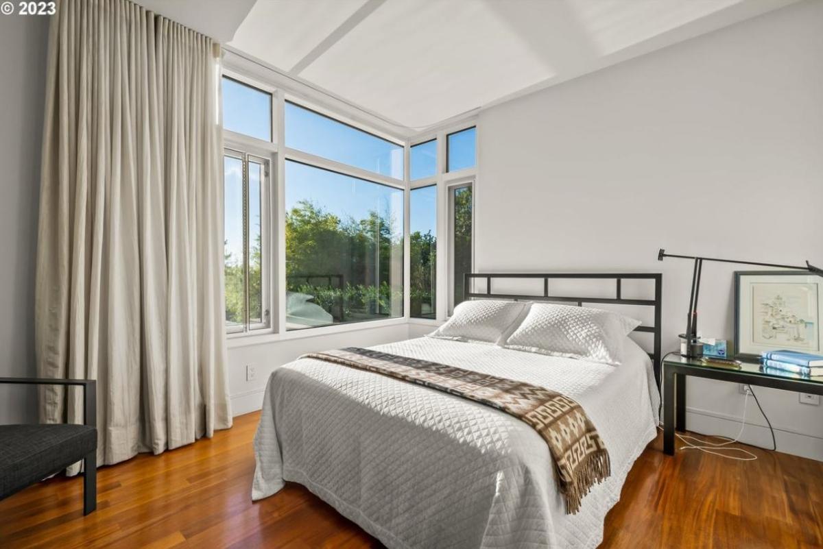 Bedroom with a large bed, wood flooring and glass windows.