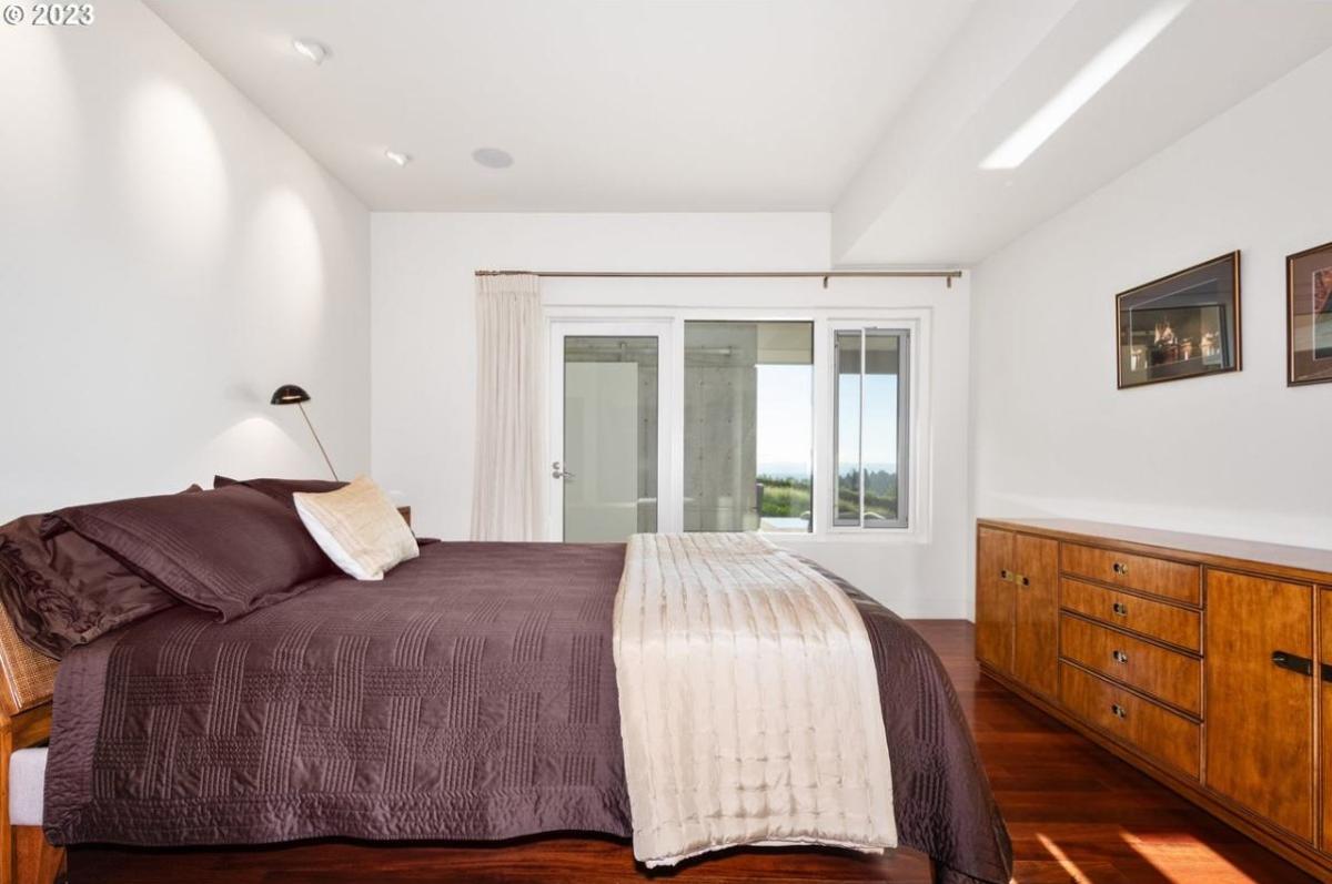 Bedroom with a large bed, wood flooring and glass windows.