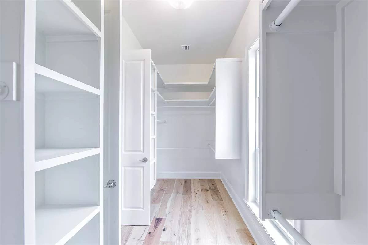 Primary walk-in closet with white built-ins and a hardwood floor.