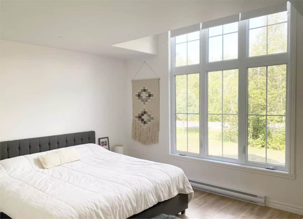 Primary bedroom with a tufted bed and a trio of windows overlooking the lush yard.