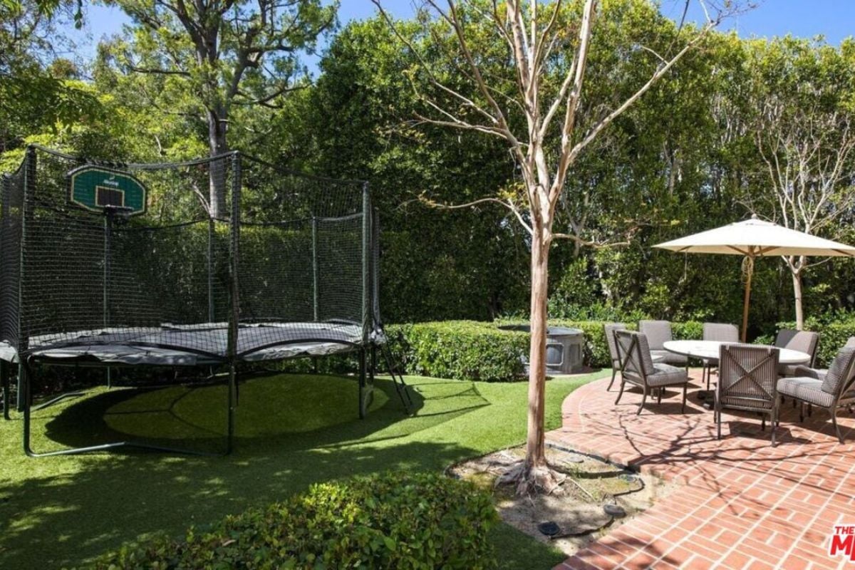 A backyard with a trampoline, table, and chairs.