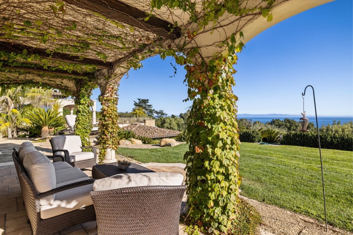 A terrace with chairs, a table, and a ceiling covered by plants.