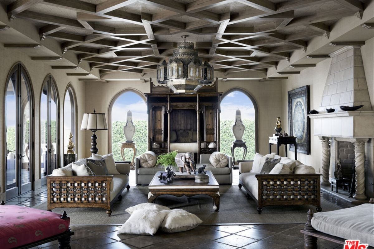 The living room, adorned with a fireplace, showcases a chandelier, couch, coffee table, pillows, vase, ceiling fixture, window, floor, and other furniture items.