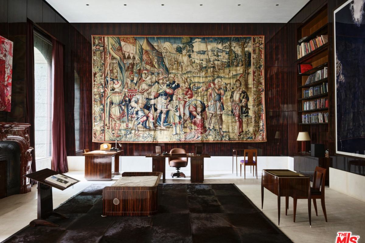 A home office with a wooden table, chairs, bookshelf, and artwork hanging on the wooden wall.