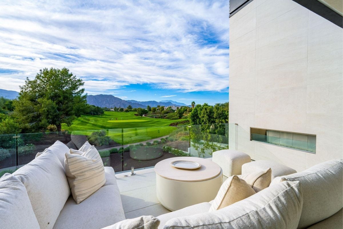 A balcony adorned with a white coffee table surrounded by white couches with white pillows.