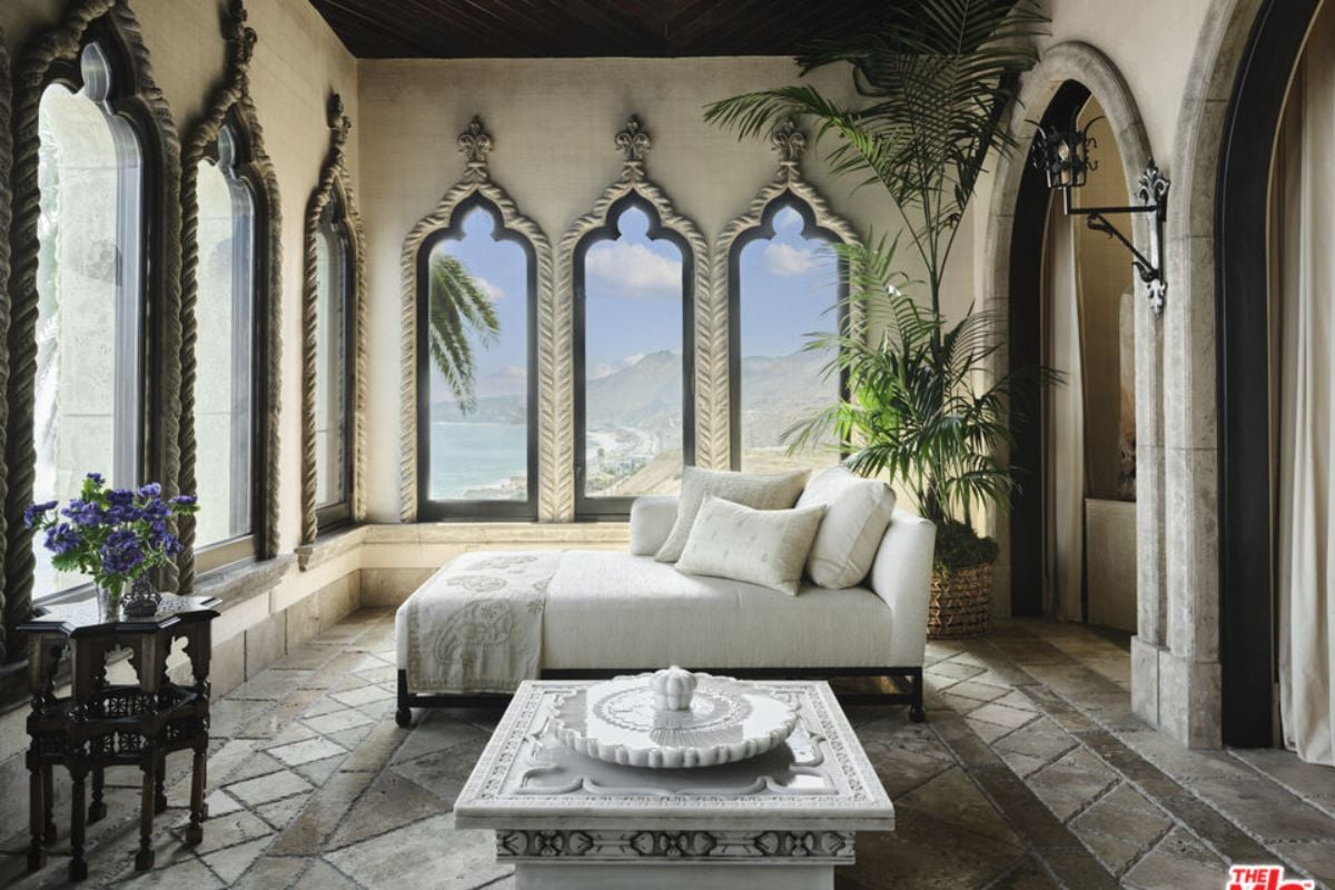 A bedroom with numerous windows, a bed positioned in the center, and a potted plant.