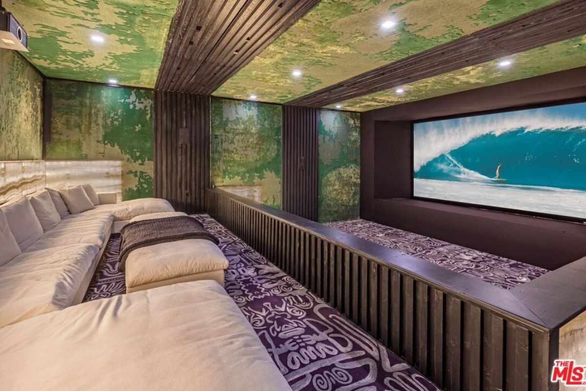 A home theater with moss green walls and ceiling, featuring a large couch and a large screen.