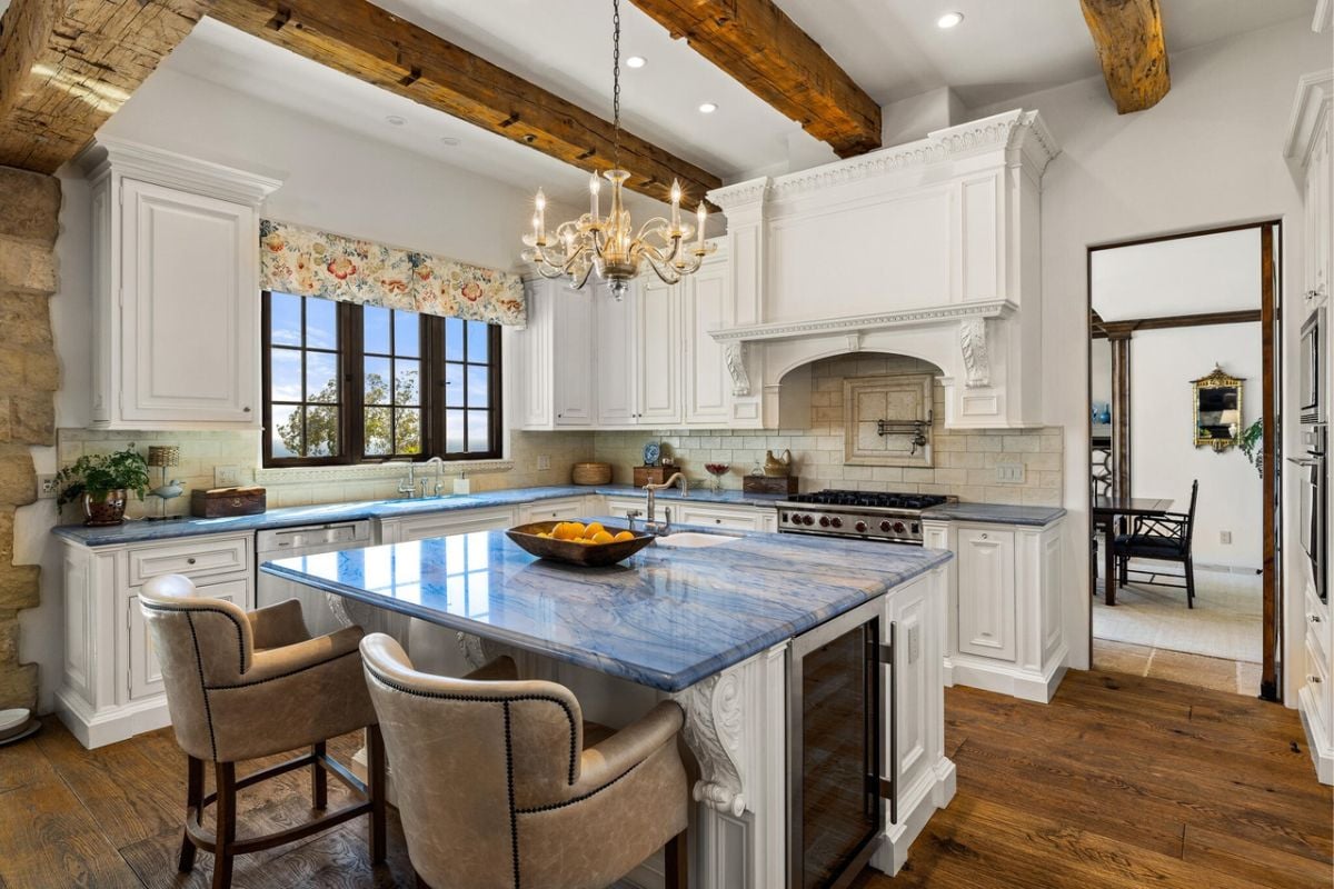 A kitchen with a large island, white walls, countertops, cabinetry, a sink, and a stove.