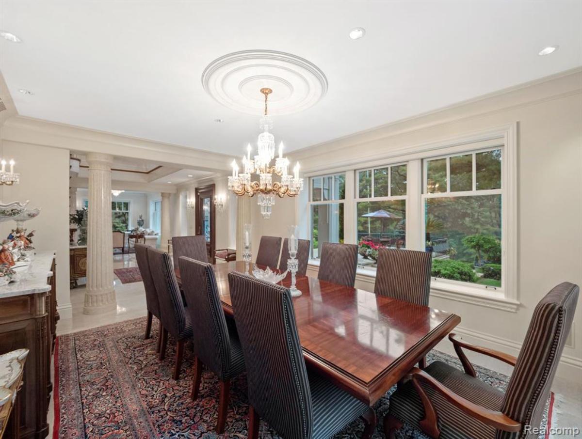 Dining room with a large table, chairs, chandelier, large rug and glass doors.
