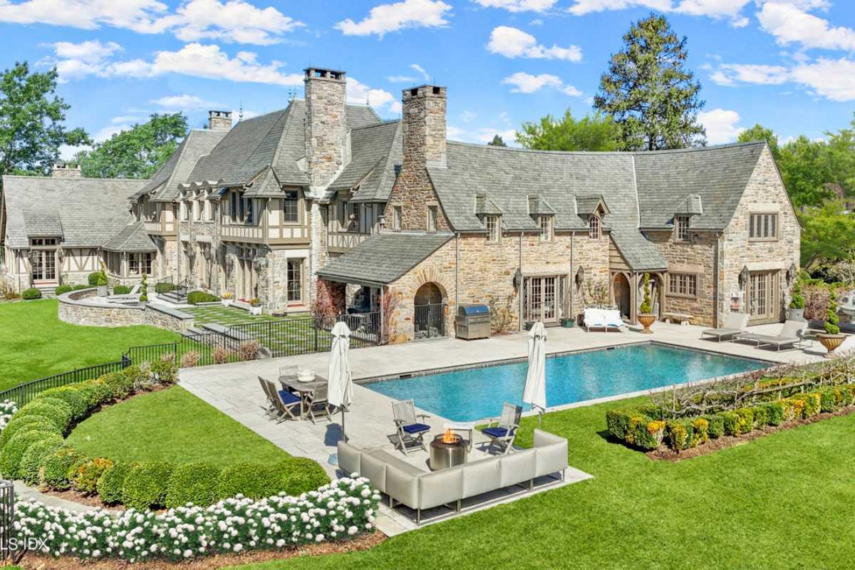 A swimming pool with chairs, a table, and a couch at the poolside.