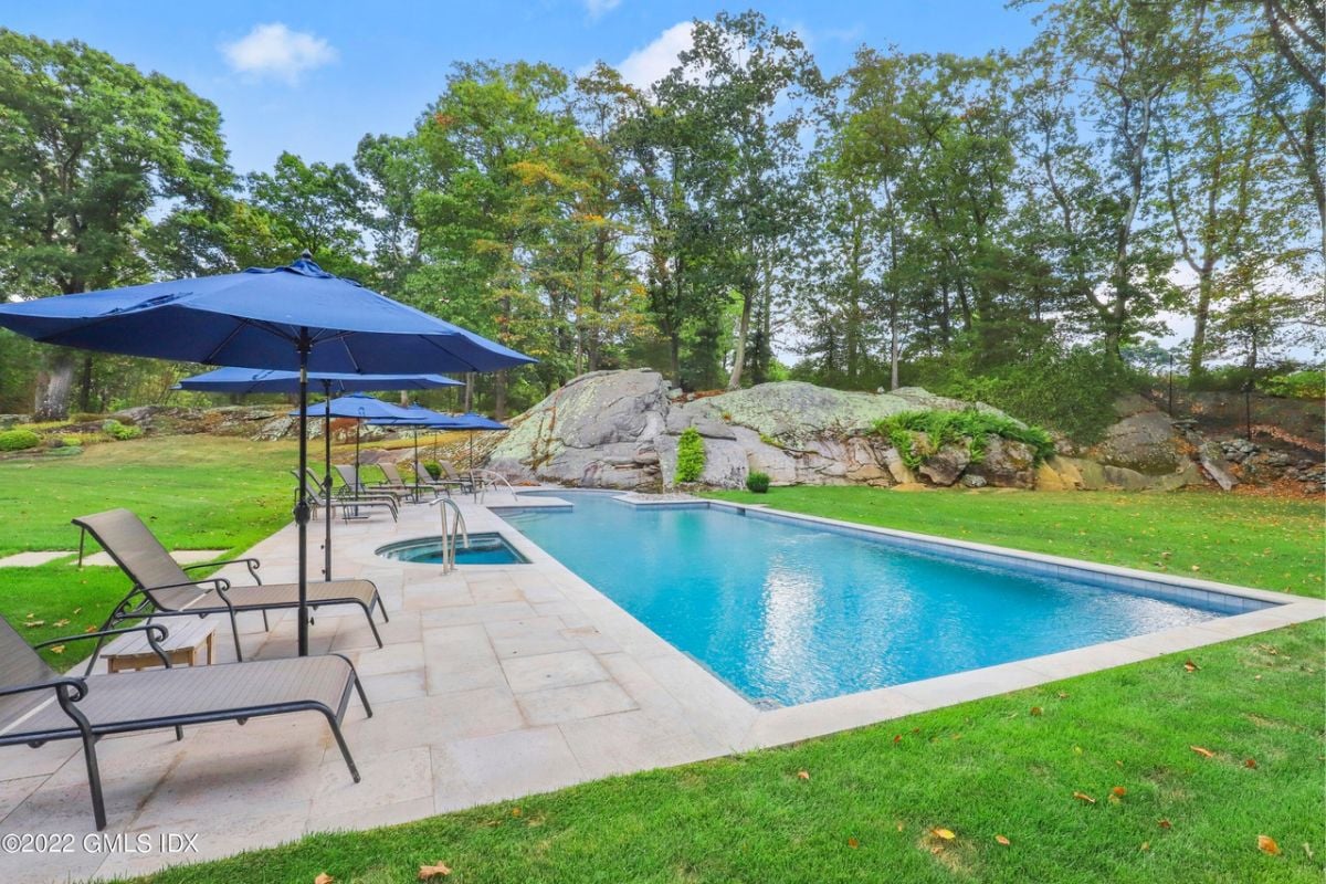 A swimming pool with chairs on the poolside, surrounded by lush green grass.