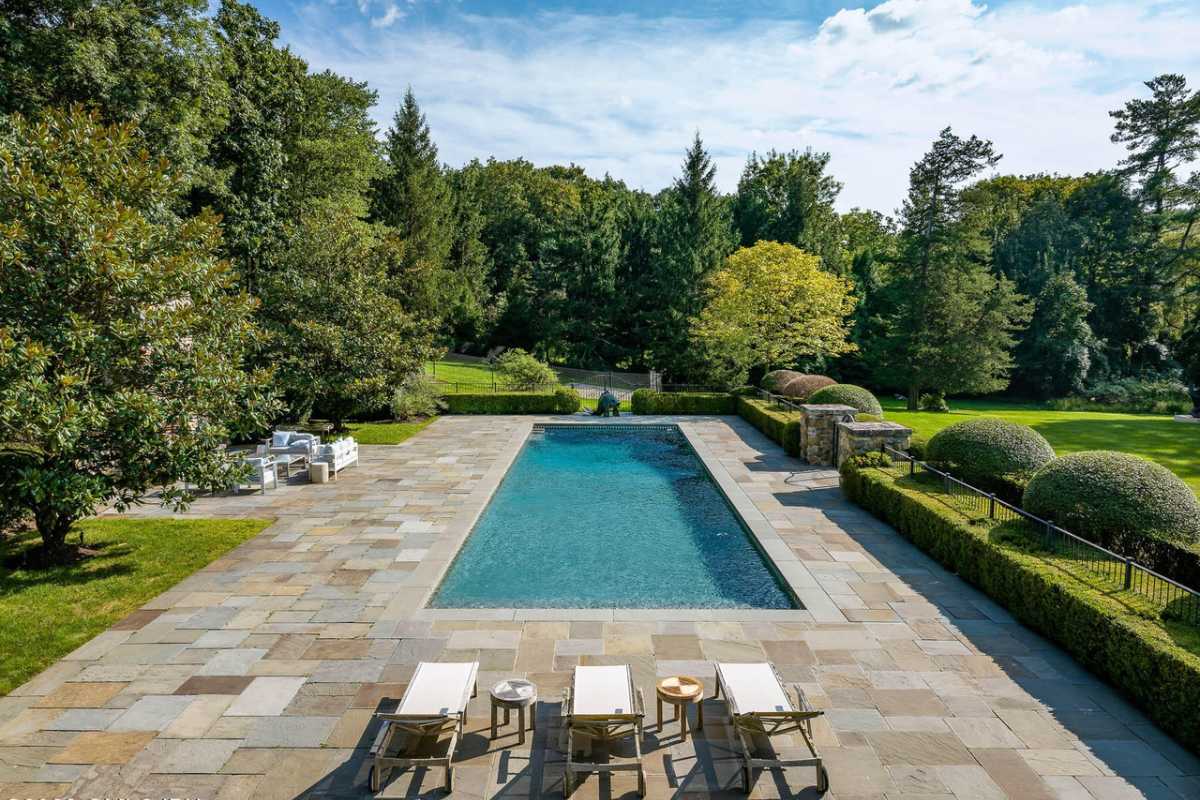 A swimming pool with tiled poolside and chairs.
