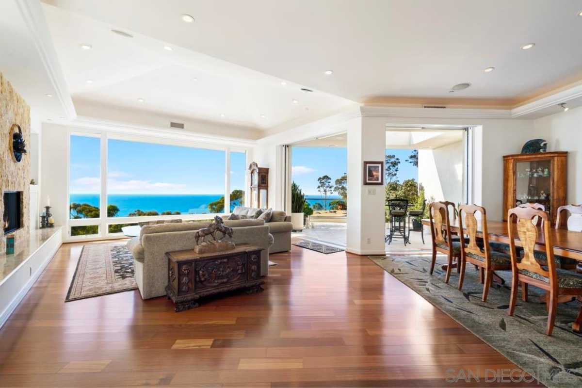 A living room with wooden floor, rug, window, white ceiling, TV, and couches.