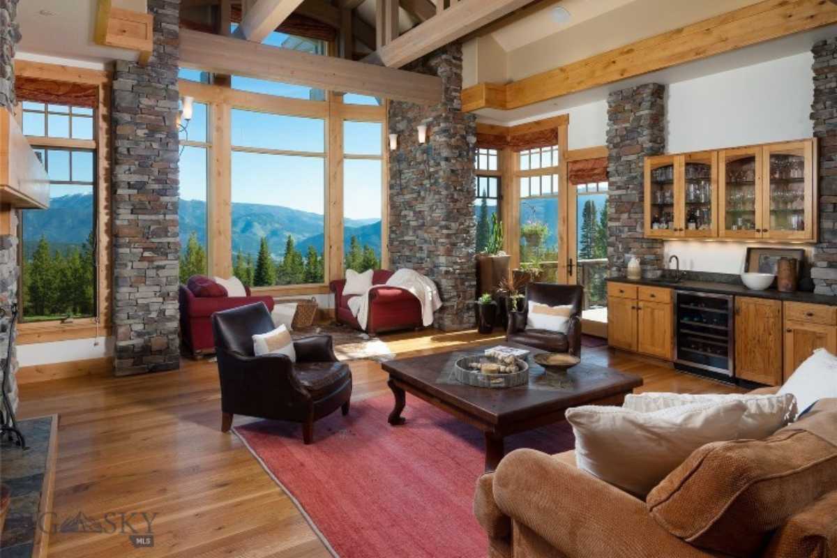 Living room with stone walls, exposed beam ceiling, windows, wooden floor, rug, couches, center table, and cabinets.