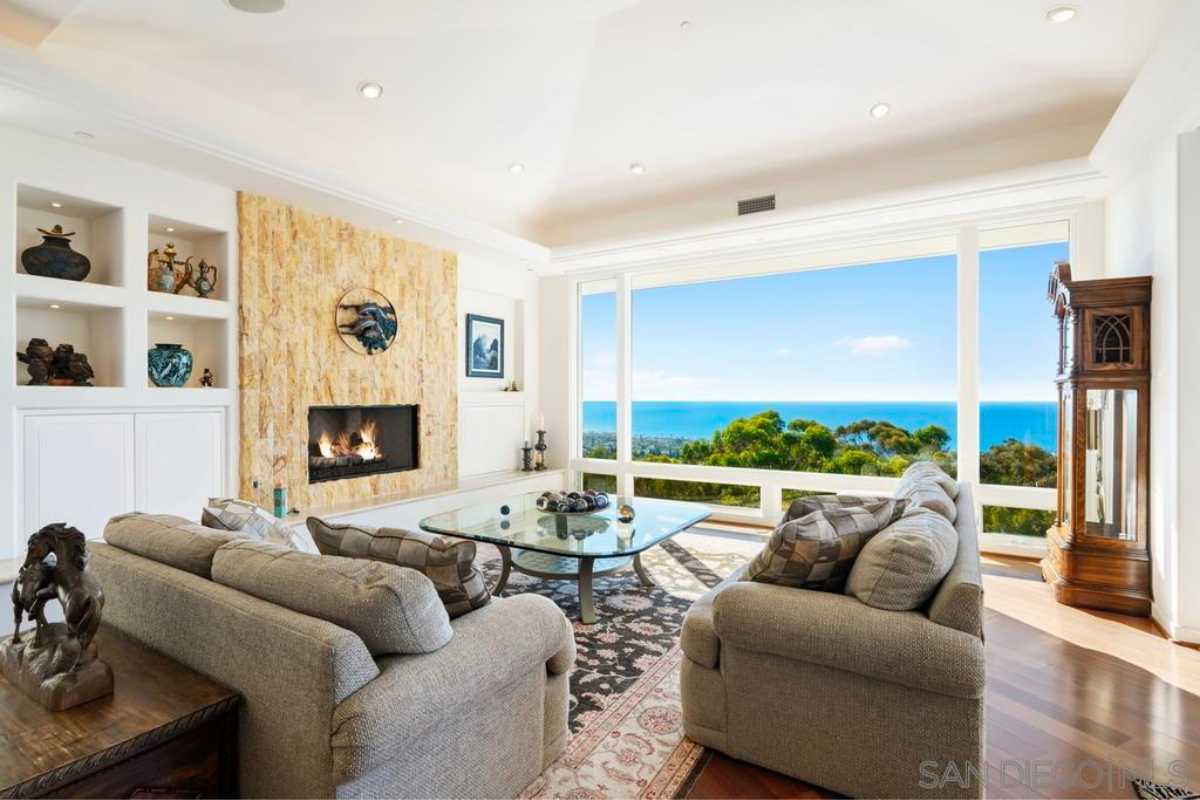 A living room with wooden floor, rug, window, white ceiling, fireplace, center table, and couches.