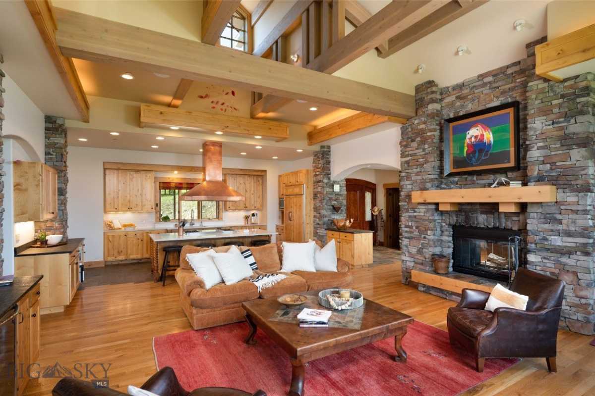 Living room with a fireplace, painting, stone walls, exposed beam ceiling, windows, wooden floor, rug, couches, center table, and cabinets.
