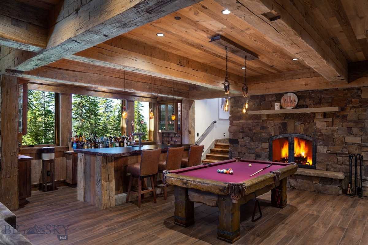 A bar with a beamed ceiling, fireplace, countertop, chairs, and pool table.