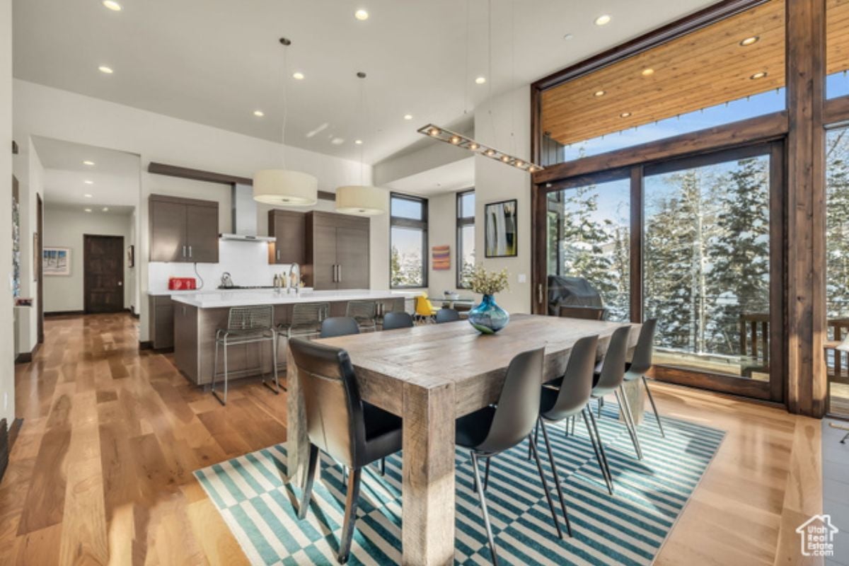 A dining room with a rug, wooden floor, white ceiling, and a dining table surrounded by chairs.