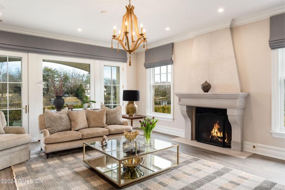 A living room with a fireplace, rug, chandelier, white ceiling, couch, and glass center table.