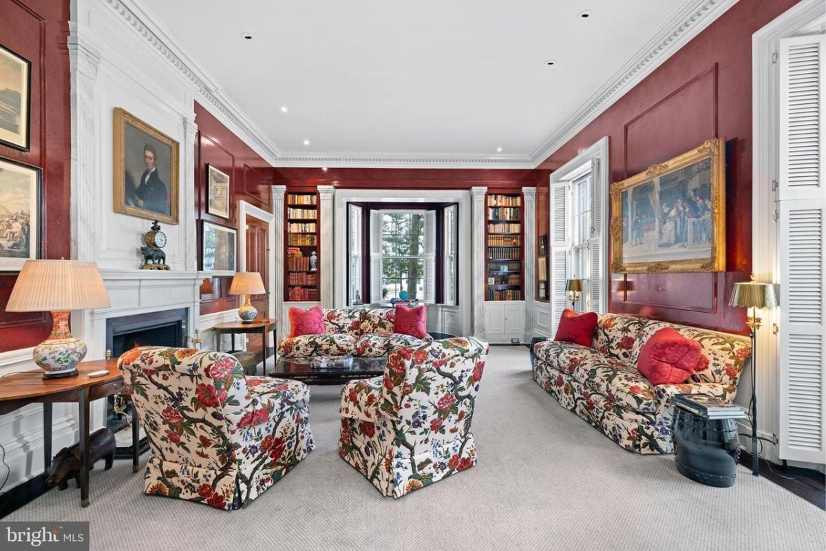 A lounge with couches, pillows, fireplace, paintings, and a white ceiling.