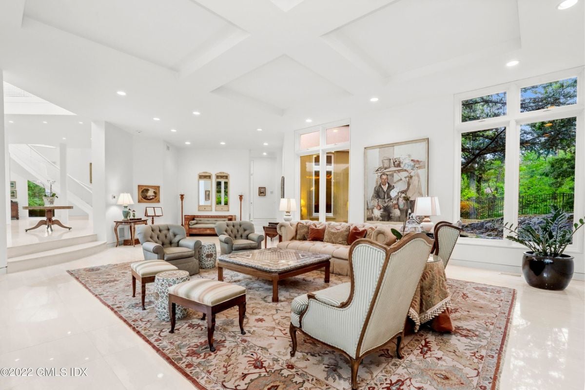 A living room with a tiled floor, rug, couch, chairs, center table, vase, white walls, and a white ceiling.