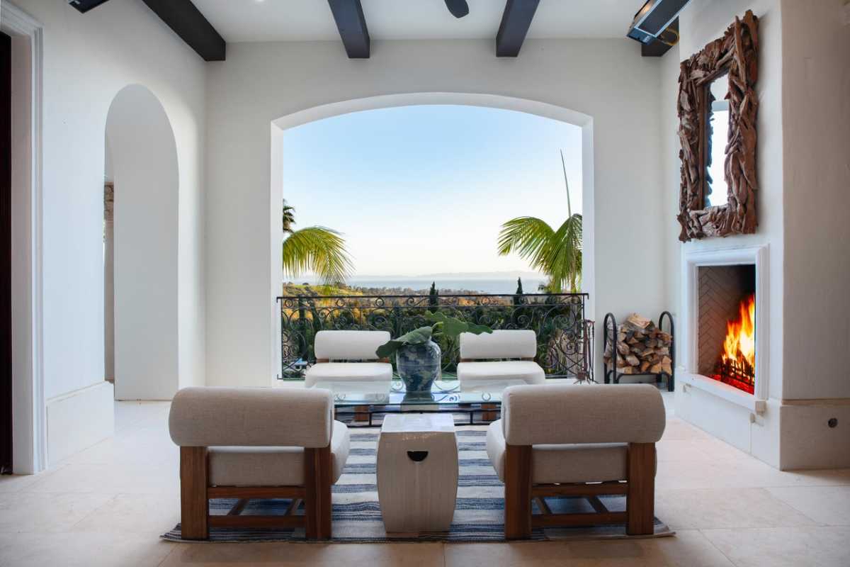 A covered porch with a couch, a coffee table, a fireplace, and a beamed ceiling.