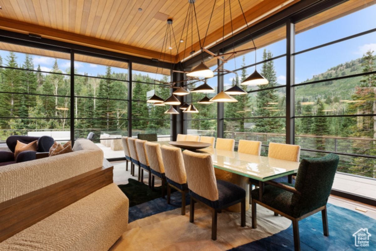 A dining room with glass walls, wooden ceiling, and a dining table surrounded by chairs.