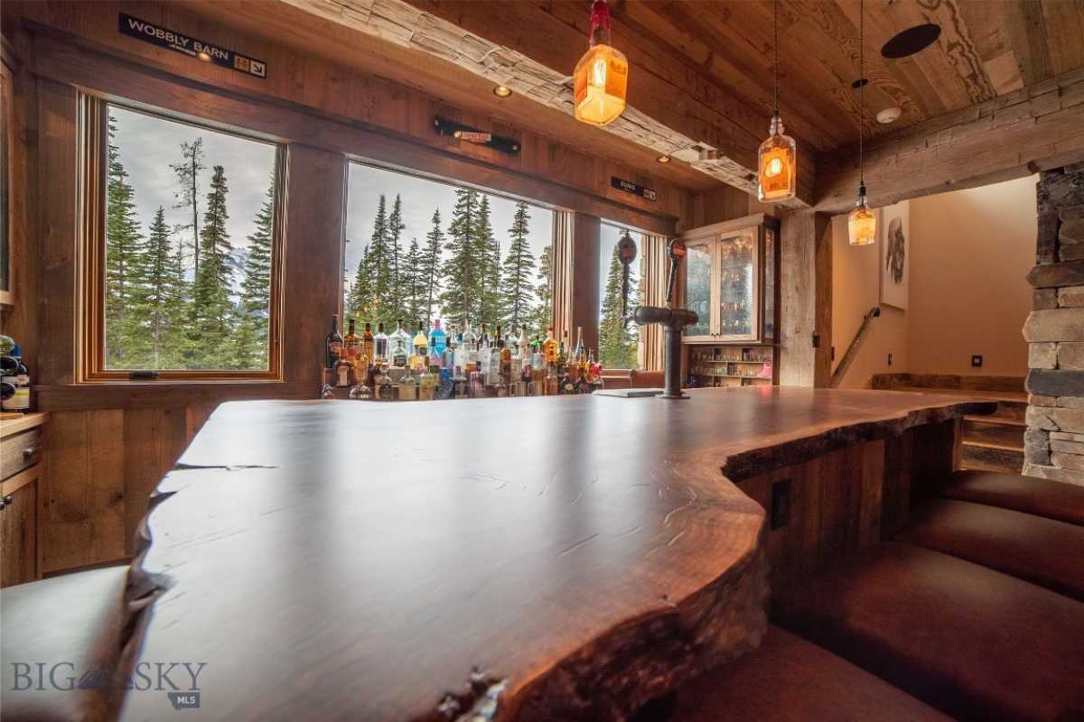 A bar with a beamed ceiling, windows, lighting, and a wooden countertop.