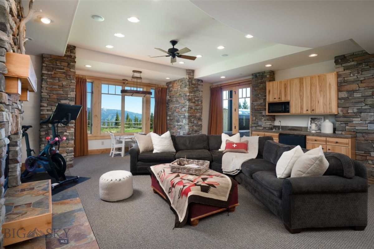 A great room with a fireplace, stone walls, windows, white ceiling, ceiling fan, dining area, living space, and kitchen.