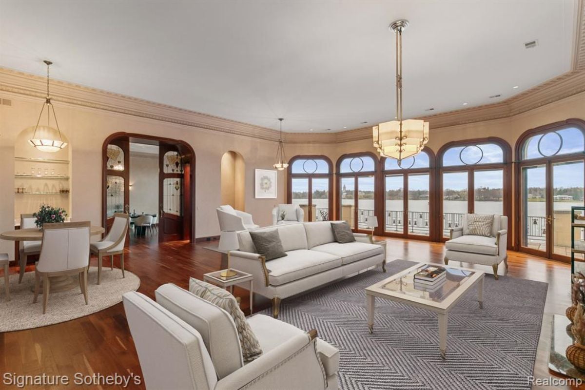 A living room with a chandelier, windows, white couches, rug, center table, and white ceiling.