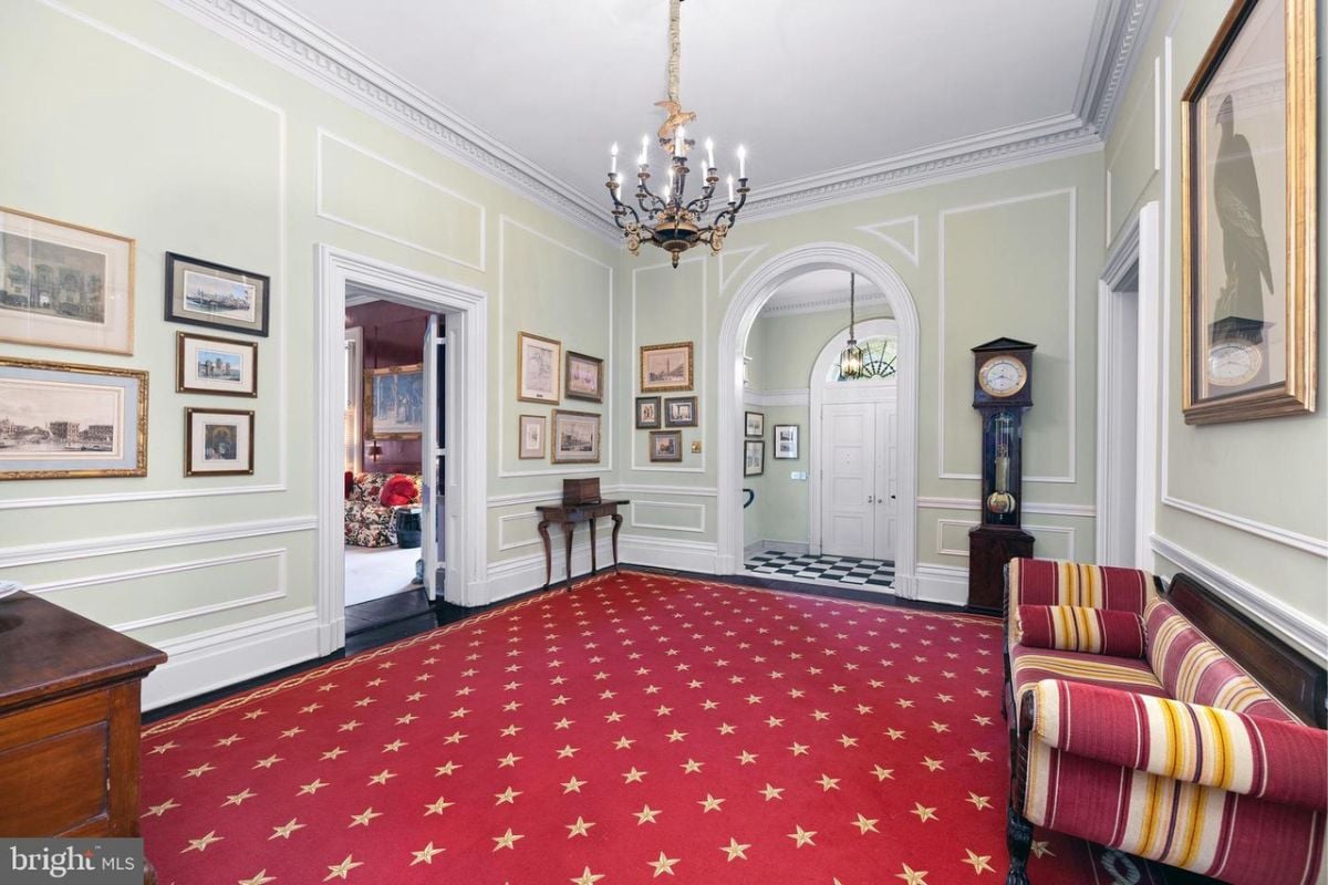 A seating area with red floor, couch, chandelier, white walls, and white ceiling.