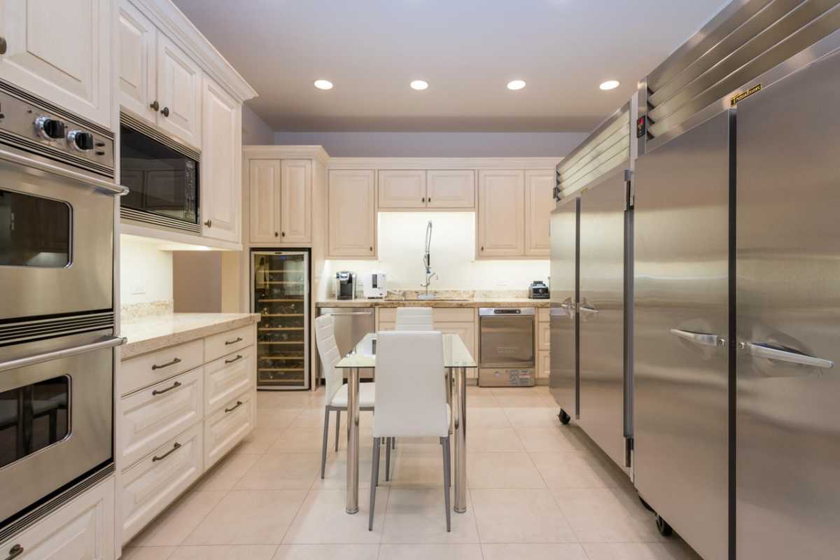 A kitchen with a table and chairs, white ceiling, white cabinets, and kitchen appliances.