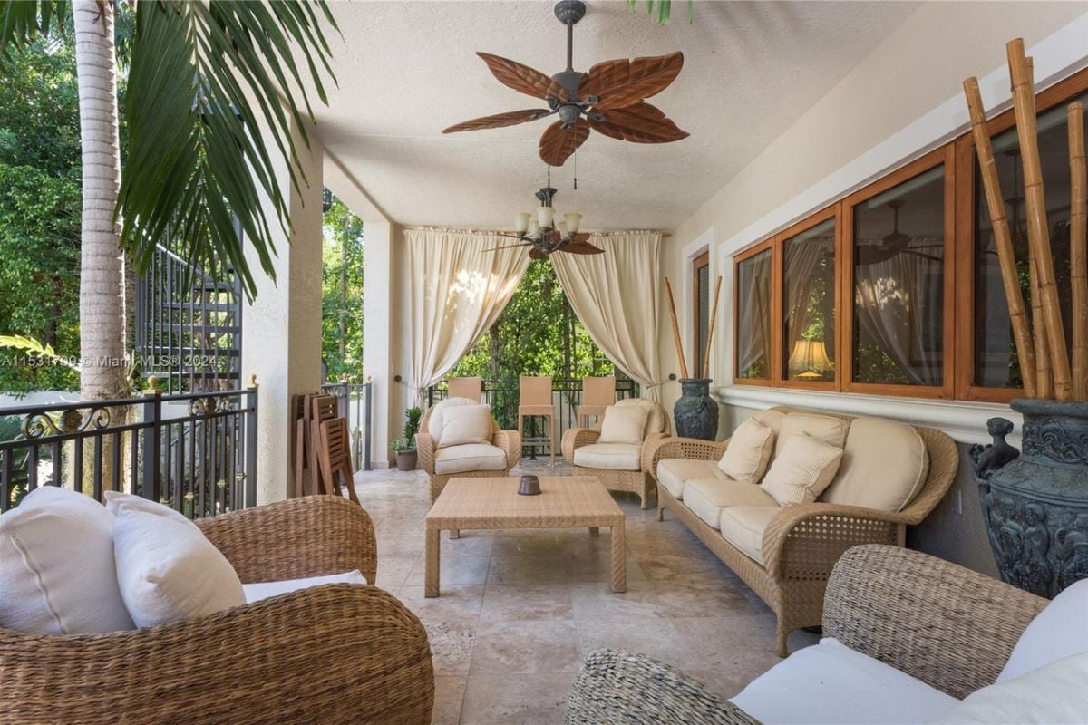 A porch with a tiled floor, a ceiling fan, a white ceiling, a center table surrounded by chairs and a couch.