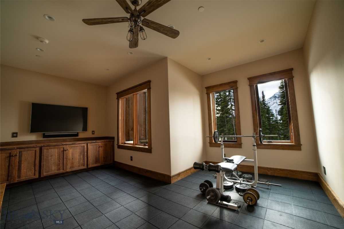 A home gym with a tiled floor, windows, ceiling fan, cabinet, and TV.