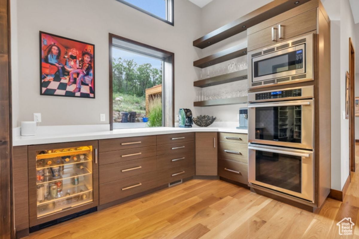 A kitchen with wooden floor, cabinets, window, and kitchen appliances.