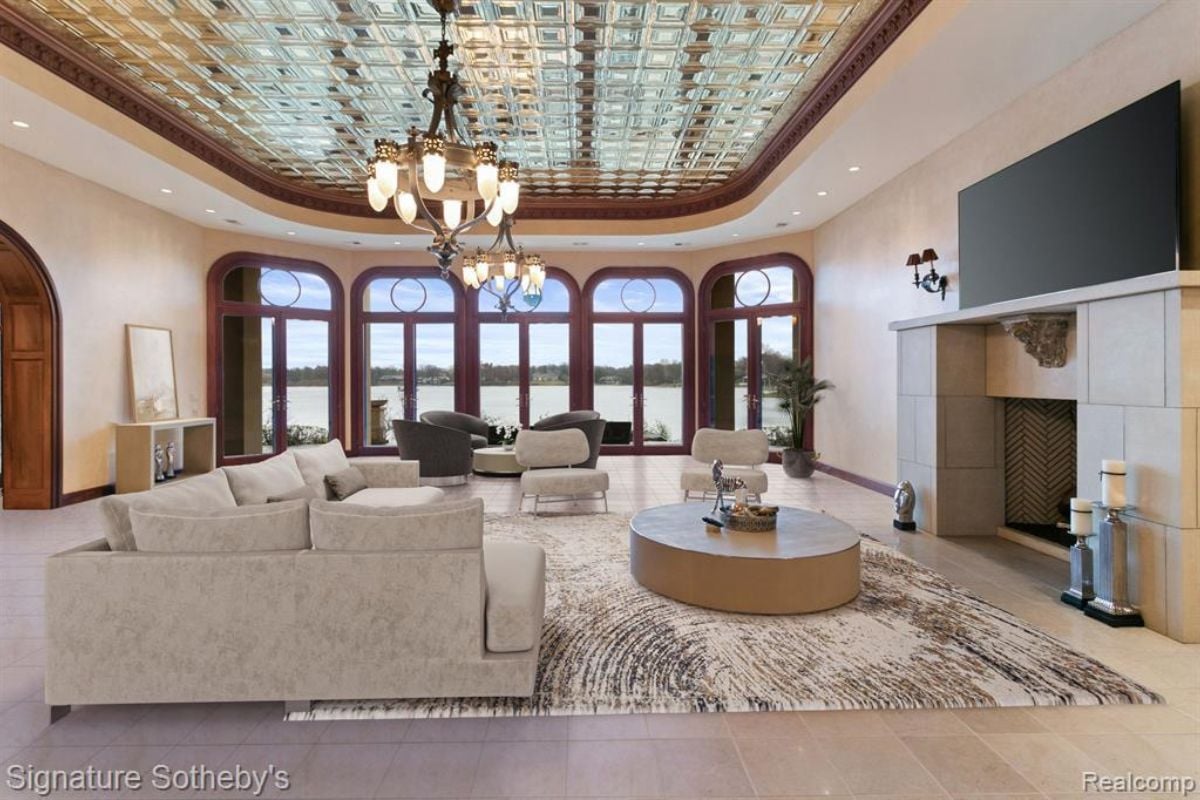 A lounge with windows, a glass ceiling, a couch, a center table, a rug, a TV, and a chandelier.