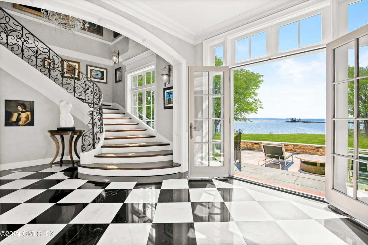 A foyer with a checkered floor, a painting, a white ceiling, and a staircase.
