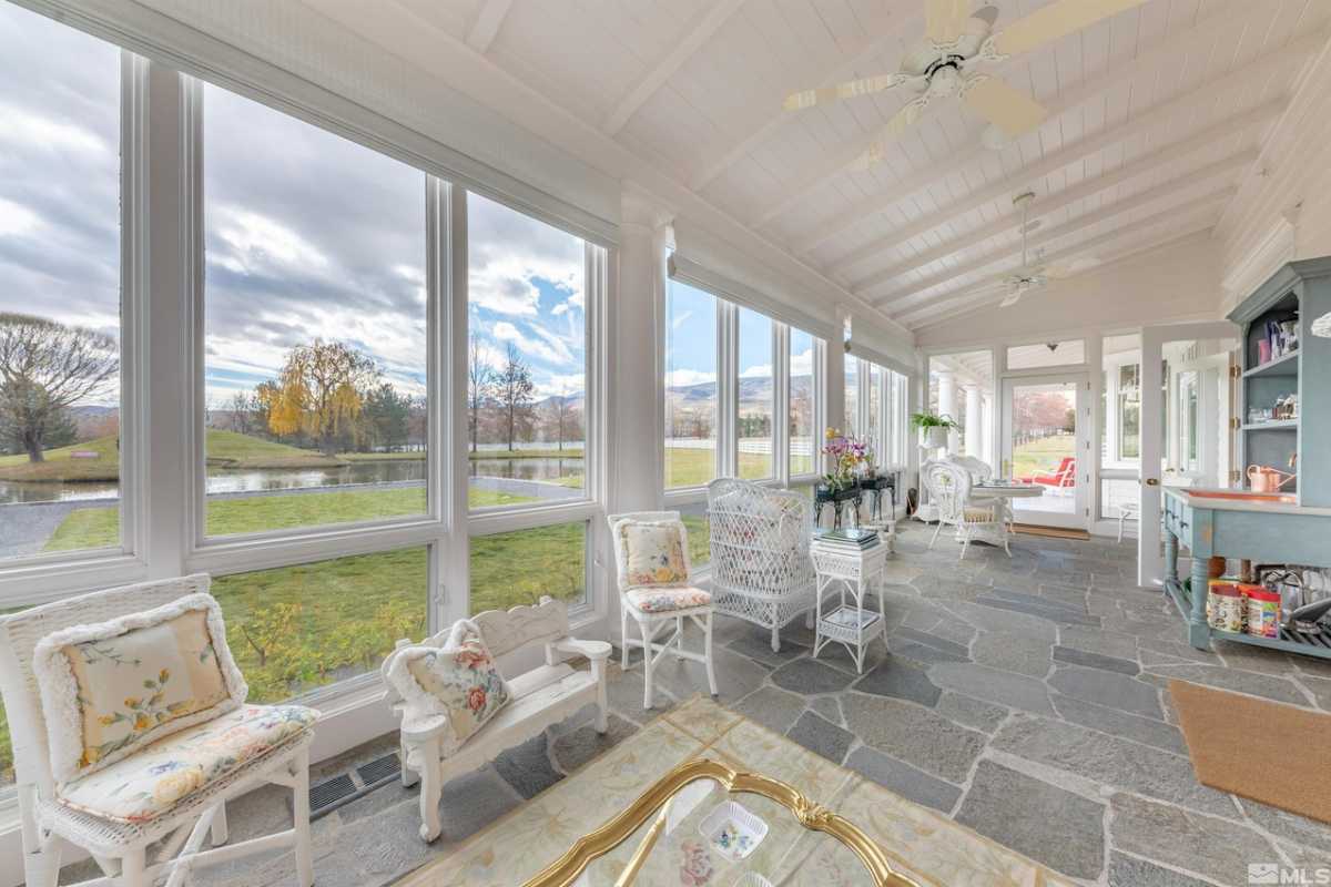 A covered porch with a stone floor, chairs, and a white ceiling.
