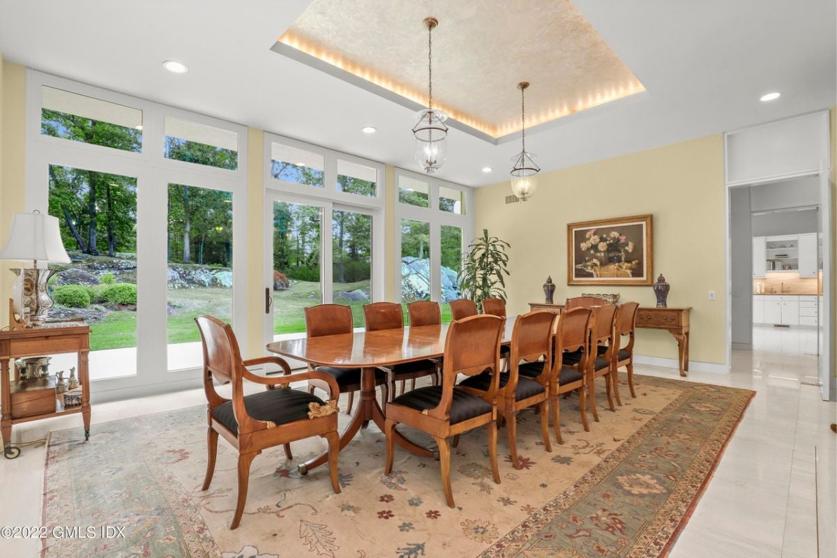 A dining room with a rug, tiled floor, white ceiling, and a long dining table surrounded by chairs.