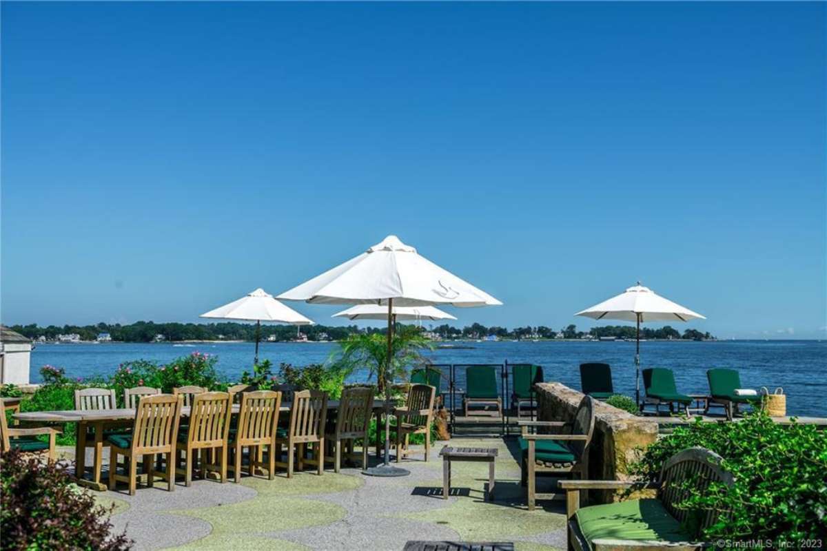 A patio with a long table surrounded by chairs, benches, tables, and an umbrella.