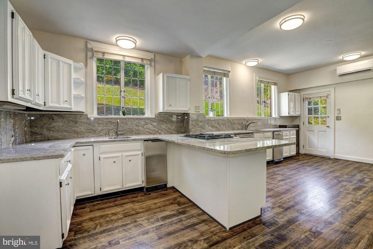 A kitchen with a wooden floor, countertop, sink, cabinets, and lighting.