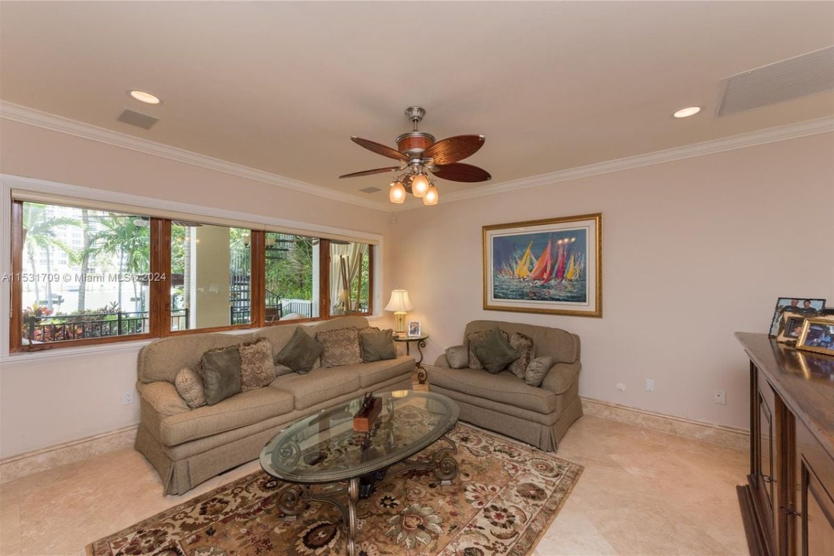 A living room with a couch, rug, glass center table, white walls, a white ceiling, and a painting.