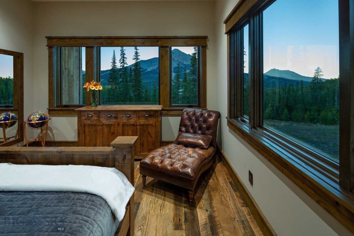 A bedroom with a bed, chair, cabinet, wooden floor, and windows.