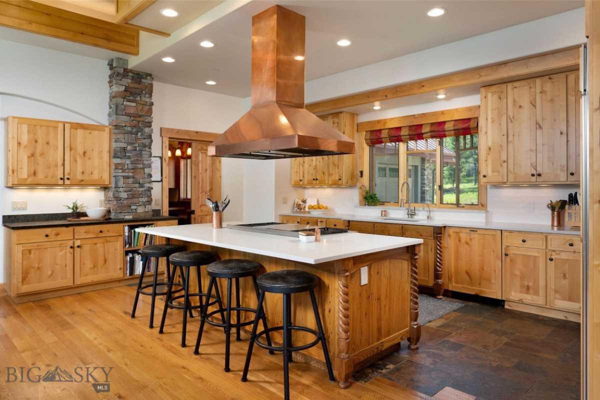 A kitchen with a wooden floor, countertop, chairs, sink, windows, and wooden cabinets.