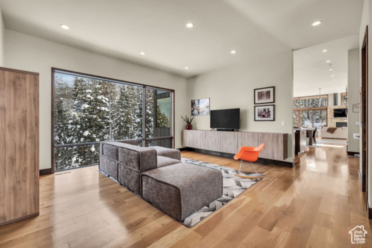 A lounge with a wooden floor, white ceiling, window, couch, rug, and TV.
