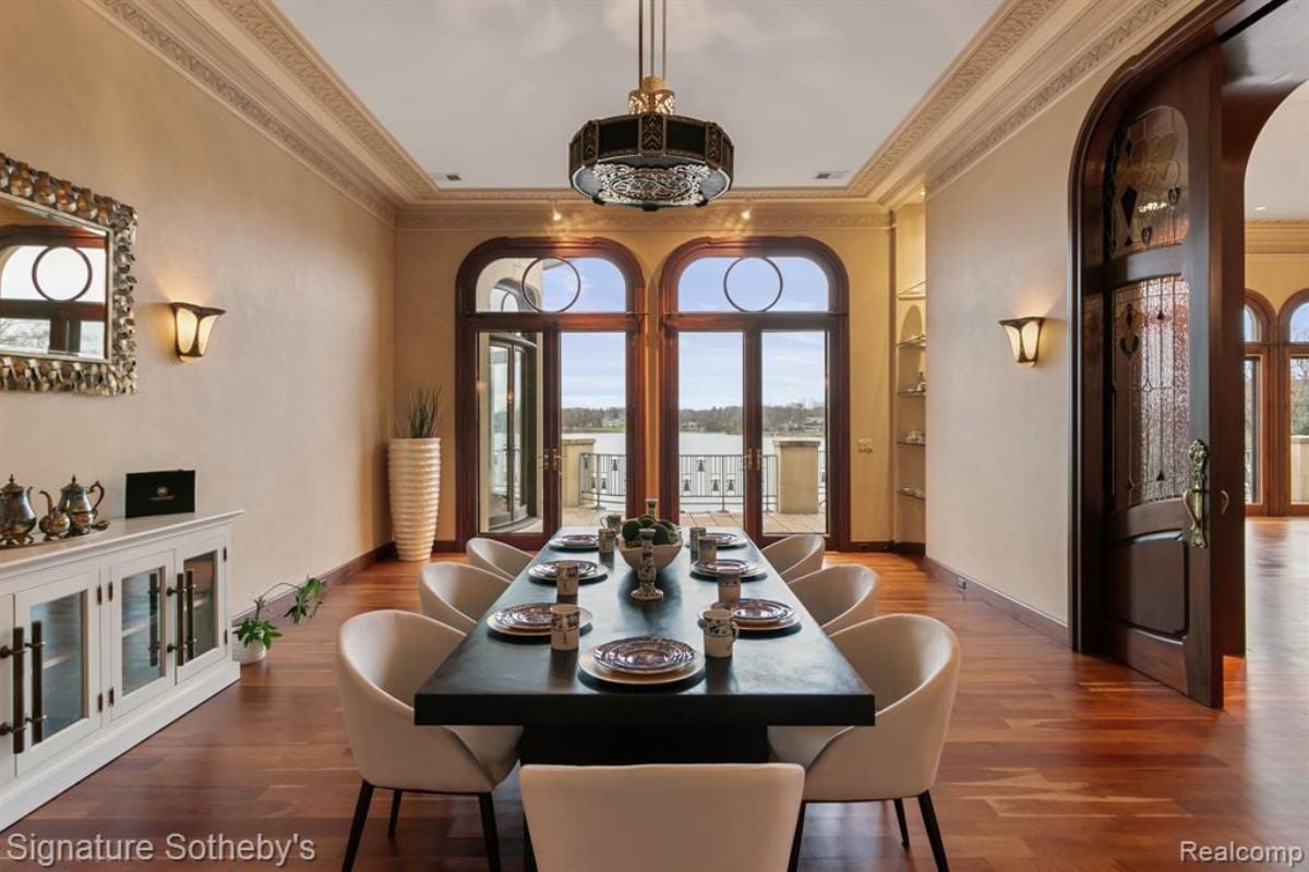 A dining room with a wooden floor, a chandelier, a wooden dining table surrounded by chairs.