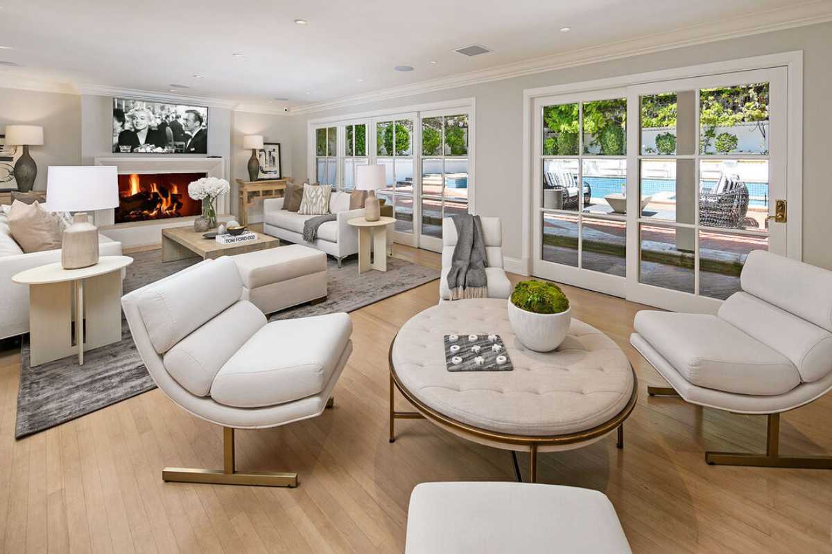 A living room with a fireplace, TV, wooden floor, windows, a white piano, a white ceiling, a rug, white couches, and a coffee table.