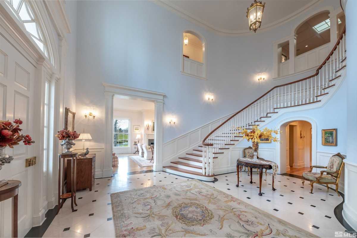 A foyer with a staircase, tiled floor, rug, white walls, chairs, and a table.